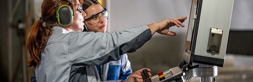 Two female CNC operators pointing at machine control panel