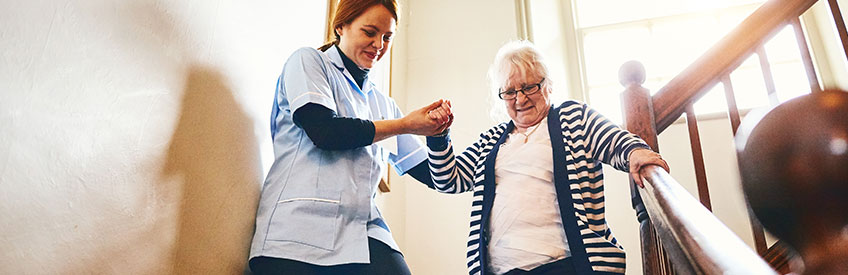 Caregiver helping senior woman walking down stairs